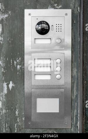 gray iron intercom with call buttons and a camera with a speaker outdoor security system on the facade of the building at the entrance close-up, nobod Stock Photo