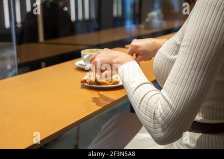 woman cuts croissant and drinks coffee at a table in a cafe. no face Stock Photo