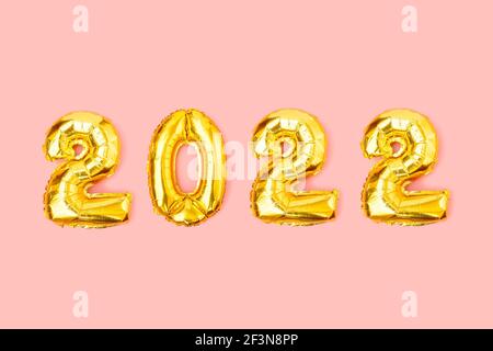 Foil balloons in form of numbers 2022. Happy New Year celebration concept. Gold balloons isolated on pink background. Flat lay, top view Stock Photo