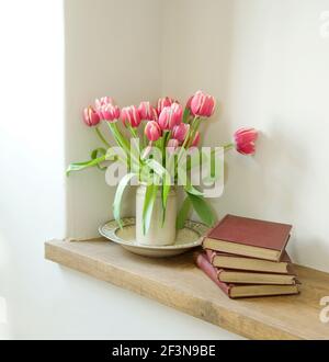 Vase of tulips and old books on a shelf. Stock Photo