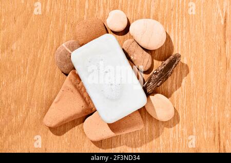 White bar of soap with bubbles on several pebbes on wooden table Stock Photo