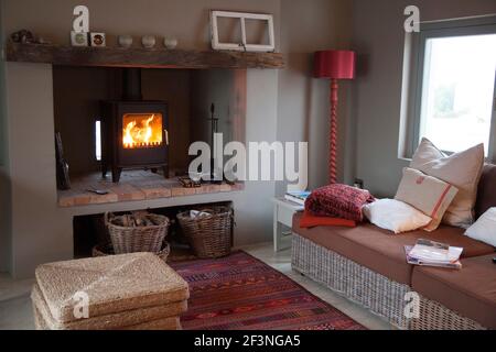 Closer view of Lounge with wood burning stove fire, cane furniture with neutral cushions and touches of red and burnt oranges in decoration details of Stock Photo