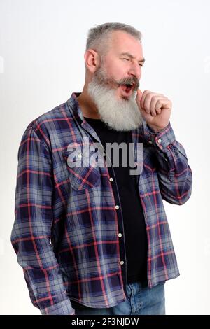 Portrait of sleepy mature bearded man in casual clothes yawning and covering mouth with hand, feeling exhausted, lack of sleep. I need rest concept on Stock Photo