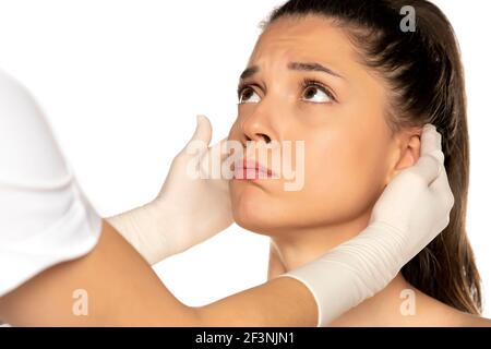 doctor's hands in gloves checks the ears of young unhappy woman on white background Stock Photo