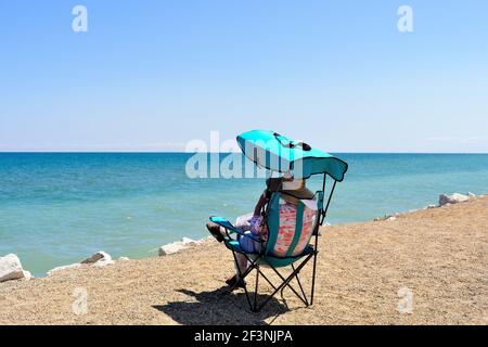 A lone woman relaxes in the sand among the dunes and above the surf at Illinois Beach State Park at Zion, Illinois. On the shore of Lake Michigan the Stock Photo