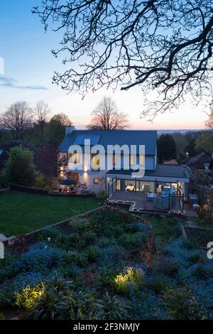House from the rear at dusk showing the terrace, extension and garden. A modern famly house with large full length glass panels. Lights in the twiligh Stock Photo