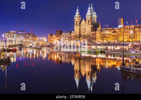 Amsterdam, Netherlands city center view with riverboats and the  Basilica of Saint Nicholas at night. Stock Photo