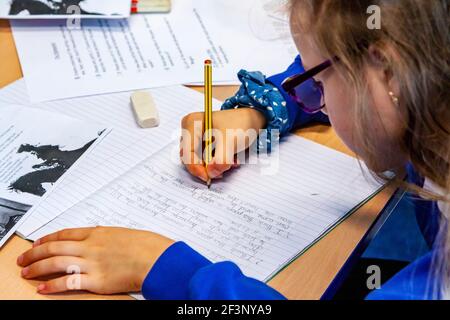 Primary school child writing on a desk during a lesson. Stock Photo