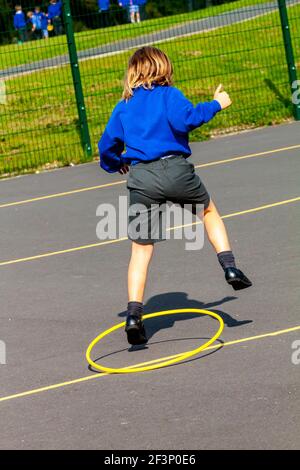 Primary school child playing with hoop outside in a school playground during a break from lessons. Stock Photo