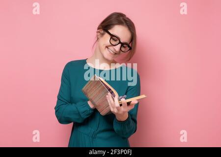 Young woman reading book smiling. Studio shot on pink wall. Stock Photo