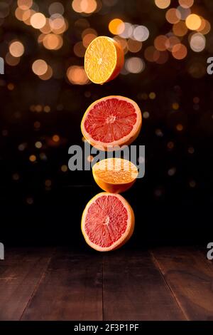 creative image of ripe orange and grapefruit slices falling on brown rustic wooden table with bokeh lights in the background Stock Photo