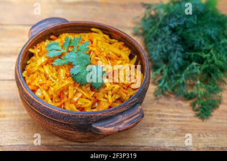 Braised cabbage, stewed with tomato sauce, served in a bowl on wooden table with green onion, parsley and dill Stock Photo
