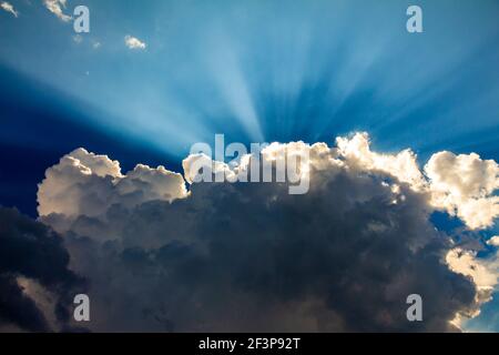 Sun rays on blue sky, behind fluffy clouds Stock Photo