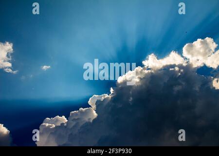 Sun beams rising behind white clouds in blue sky Stock Photo