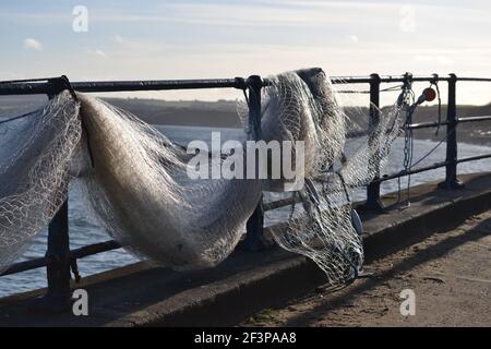 Fishing Net Hanging On Metal Safety Rails Along Filey Seafront - White Fishing Net Drying Out - Blue Sky And A Calm North Sea - Filey Bay - Yorkshire Stock Photo