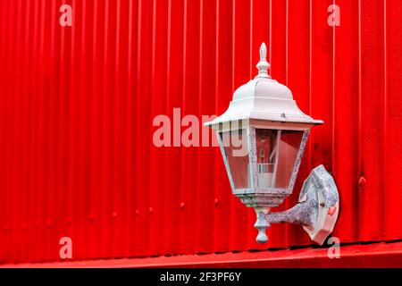 Corrugated ribbed red painted peeling paint wall of abstract architecture building with electric bulb lamp lantern outside on house in Reykjavik, Icel Stock Photo