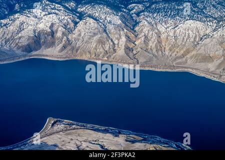 Aerial view of the coastline of British Columbia with a train travelling along the bright blue water of the pacific ocean and rugged landscape Stock Photo