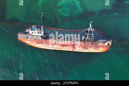 The old rusty ship was stranded by a storm. Oil spill from a tanker, environmental pollution. Stock Photo