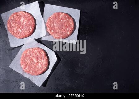 Three raw beef patties for burger on the black background, close up, flat lay. Stock Photo