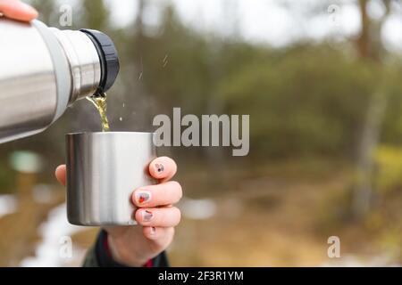 Youg beautifull women pouring beverage from termos to cup in a cold raini day. Healthy living and hiking. Stock Photo