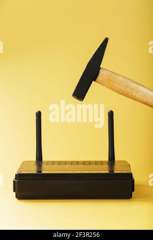 A hammer hits the Wi-Fi modem router to break it against a yellow ...