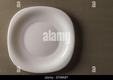 Close up view of white  square shaped plate on brown background. Brown and white background. Eating concept background. Stock Photo