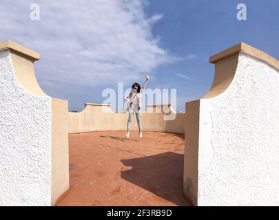 A pretty cheerful middle-aged Hispanic woman jumping on the roof of a building Stock Photo