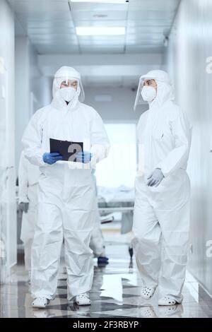 Group of doctors in protective suit walking along the corridor at hospital and talking to each other Stock Photo