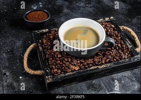 Coffee cup and beans in old wooden tray. Black background. Top view Stock Photo
