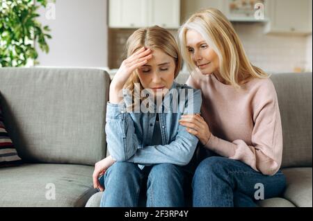 Mother and daughter together at living room. Loving mature mom sits on the couch and hugs her young adult daughter, stroking her, sympathizes, family relationship and values concept Stock Photo