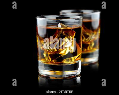Glasses of whiskey with ice isolated on black background with reflection. Close up view. Selective focus on ice. Stock Photo