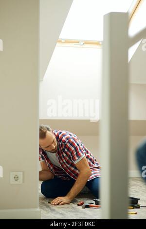 Handyman sitting on the floor while fixing smething in a room. Home repair hand tools on laminate flooring Stock Photo
