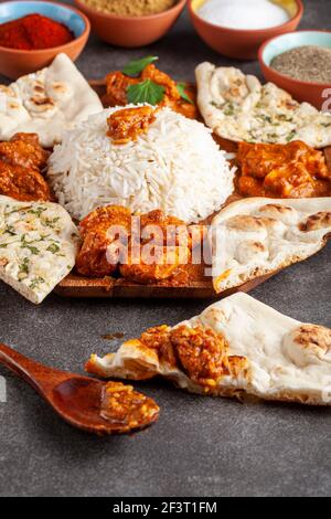 Angled image of a gourmet mixture of indian dishes including rice, naan, tikka masala, butter chicken and curry. Spices and herbs are seen in blurred Stock Photo