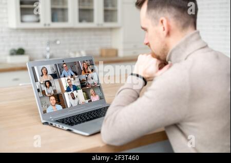 A male employee has video conference with colleagues, back view over shoulder on the laptop screen with a diverse team on it, video meeting concept Stock Photo