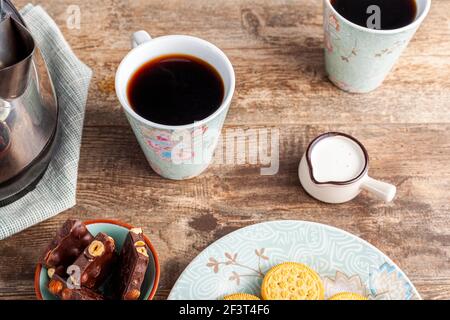 a tea time or coffee time concept with sandwich cookies, bars of chocolate aesthetic ceramic mug and plates as well as a mini creamer pitcher on woode Stock Photo