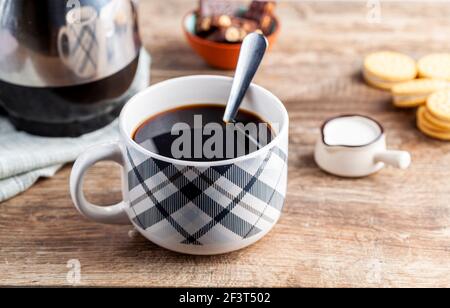 a tea time or coffee time concept with sandwich cookies, bars of chocolate aesthetic ceramic mug and plates as well as a mini creamer pitcher on woode Stock Photo