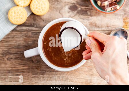 a tea time or coffee time concept with sandwich cookies, bars of chocolate aesthetic ceramic mug and plates as well as a mini creamer pitcher on woode Stock Photo
