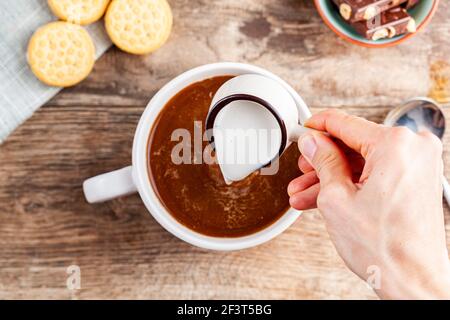 a tea time or coffee time concept with sandwich cookies, bars of chocolate aesthetic ceramic mug and plates as well as a mini creamer pitcher on woode Stock Photo