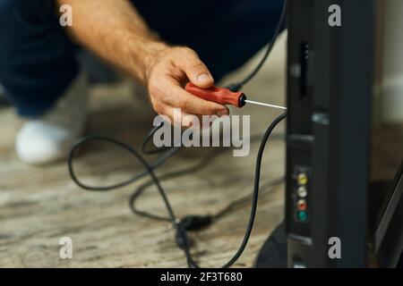 Handy home repair. Close up shot of hand of a repairman using a screwdriver while installing or fixing tv set indoors Stock Photo
