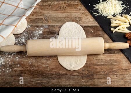 Closeup image A baker's wooden rolling pin on  a flattened dough on wood kitchen countertop. A bread making concept image with loafs and cheese and su Stock Photo