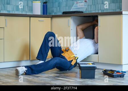 Efficient work. Professional plumber wearing tool belt fixing sink pipe indoors Stock Photo