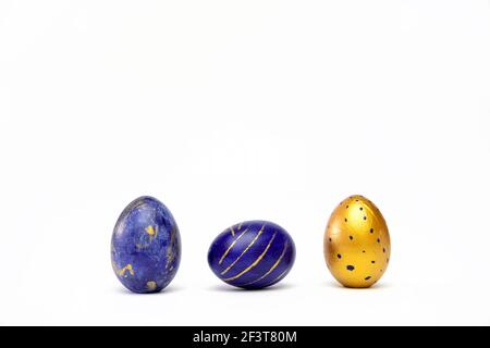 Three easter eggs trendy colored classic blue, white and golden decorated on white table. Happy Easter card with copy space for text. Minimal style Stock Photo