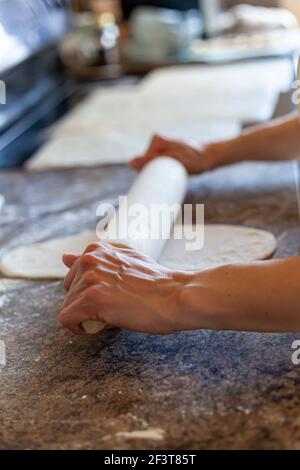 A caucasian woman is using an American rolling pin to roll over bread doughs to flatten and shape them. Authentic kitchen background homemade bread ma Stock Photo