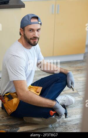 Full length shot of young repairman looking at camera, holding plumbing tools in his hands while sitting in Lotus pose on the floor indoors Stock Photo