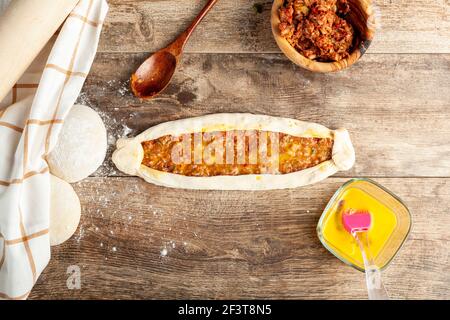 Flat lay image showing ready to bake kiymali pide, a sort of Turkish pizza or flat bread with ground beef and egg topping. Doughs, mixture bowl, homog Stock Photo