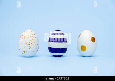 Three easter trendy colored classic blue and golden decorated eggs striped pattern on blue. Happy Easter card with copy space for text. Minimal style Stock Photo