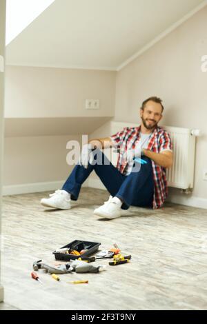 Blurred shot of cheerful handyman using pipe wrench for repairing radiator battery in the room. Home repair hand tools on laminate flooring Stock Photo