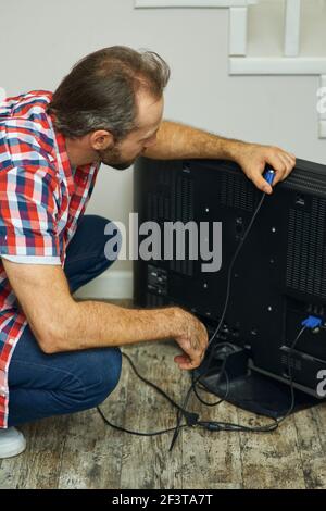 Installation process. Handyman looking focused, holding tv cable while installing or fixing tv set in apartment of a customer Stock Photo