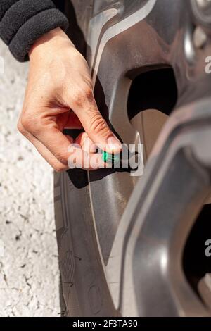 A caucasian woman is removing or attaching the green tire stem valve cap of her vehicle. This is done for checking the tire pressure and inflating whe Stock Photo