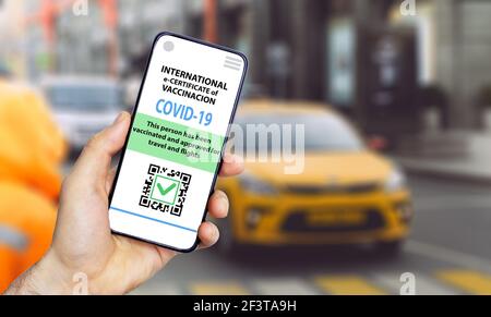 Coronavirus vaccination certificate or vaccine passport for travellers concept. COVID-19 immunity e-passport in the smartphone mobile app for international travelling. City street background. Stock Photo